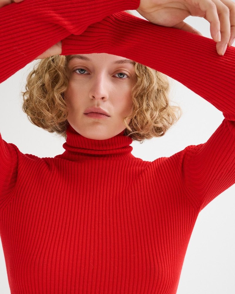 Roberto Collina — red ribbed turtleneck, hands in her hair
